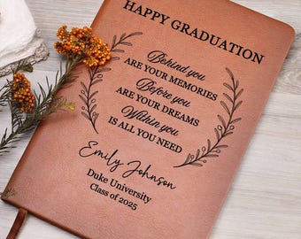 May include: A brown leather-bound graduation journal with the words "HAPPY GRADUATION" at the top. The journal is personalized with a name, university, and class year. The cover includes an inspirational quote and floral design.