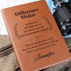 May include: A tan leather-like journal with black engraved text that reads Difference Maker, Be proud of the work you do, the person you are and the difference you make, There are people in this world who make things better, Jennifer.