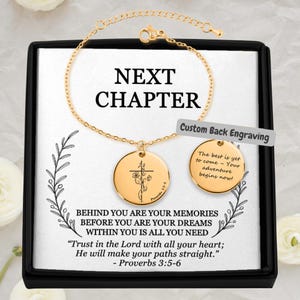 May include: Gold-colored bracelet and pendant set in a black box. The pendant features a cross and floral design, with the words "NEXT CHAPTER" above the pendant. The box also contains the text "BEHIND YOU ARE YOUR MEMORIES..." and "Trust in the Lord with all your heart..."