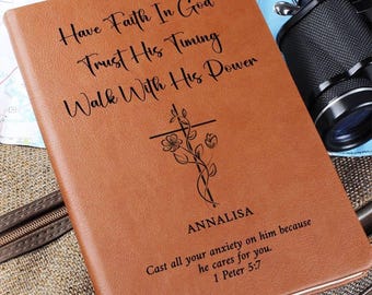 Op de afbeelding: Een bruin notitieboek in lederlook met de gegraveerde tekst Have Faith In God Trust His Timing Walk With His Power, een bloemrijke kruisillustratie, de naam Annalisa en het vers Cast all your anxiety on him because he cares for you. 1 Peter 5:7.