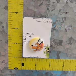 May include: A round button featuring a cartoon dog character with a yellow background, attached to a white card. The card has text that reads "Because it's from the old" and "art of the day". The button is approximately 1 inch in diameter.