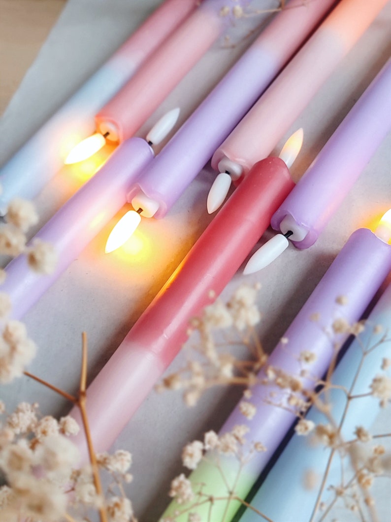 May include: Assortment of ombre taper candles in shades of pink, purple, and blue. The candles are arranged in a diagonal pattern and are lit, casting a warm glow.