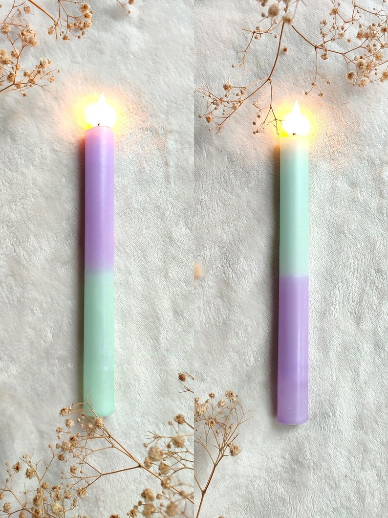 May include: Two lit candles with a gradient of purple and light green. The candles are on a white surface with dried flowers.