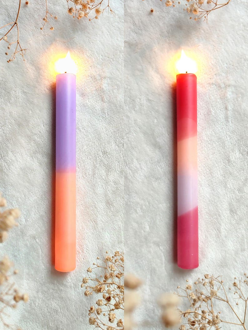 May include: Two lit candles with a gradient of colors. The candle on the left is purple and orange. The candle on the right is red, pink, and orange.