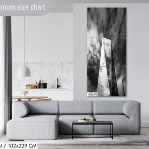 Puede incluir: Tr&iacute;ptico en blanco y negro que representa un rascacielos contra un cielo nublado. La obra de arte se exhibe sobre un sof&aacute; gris en un sal&oacute;n moderno. Las dimensiones del lienzo son 102x229 cm.