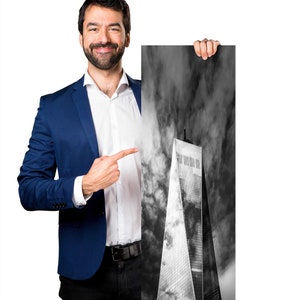 Puede incluir: Fotograf&iacute;a en blanco y negro de un rascacielos contra un cielo nublado. La imagen mide 30x91 cm. Una persona con una blazer azul y camisa blanca sostiene la fotograf&iacute;a y la se&ntilde;ala.