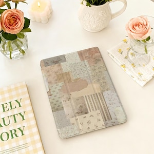 May include: A tablet case with a patchwork design in pastel colors, including beige, pink, and light blue. The case is surrounded by floral arrangements, a candle, and a book with the text "ELY BEAUTY STORY".