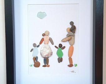 May include: Framed pebble art depicting a family of five, with a light blue cloud. The artwork features a black frame and a white mat. A large oyster shell sits in front of the framed art.