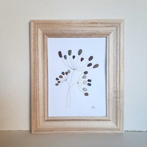 May include: A framed artwork featuring a flower made of small stones in shades of brown, green, and gray. The flower is depicted on a white background with a simple black line drawing of the stem and leaves.