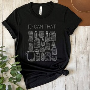 May include: Black t-shirt with white text that reads "I'd Can That" and a graphic of various jars with lids. The jars are filled with different items, such as pickles, beans, and herbs.