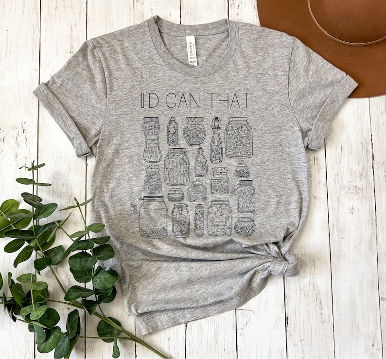 May include: A gray t-shirt with the text "I'd Can That" printed on the front. The shirt features a design of various jars filled with different items.