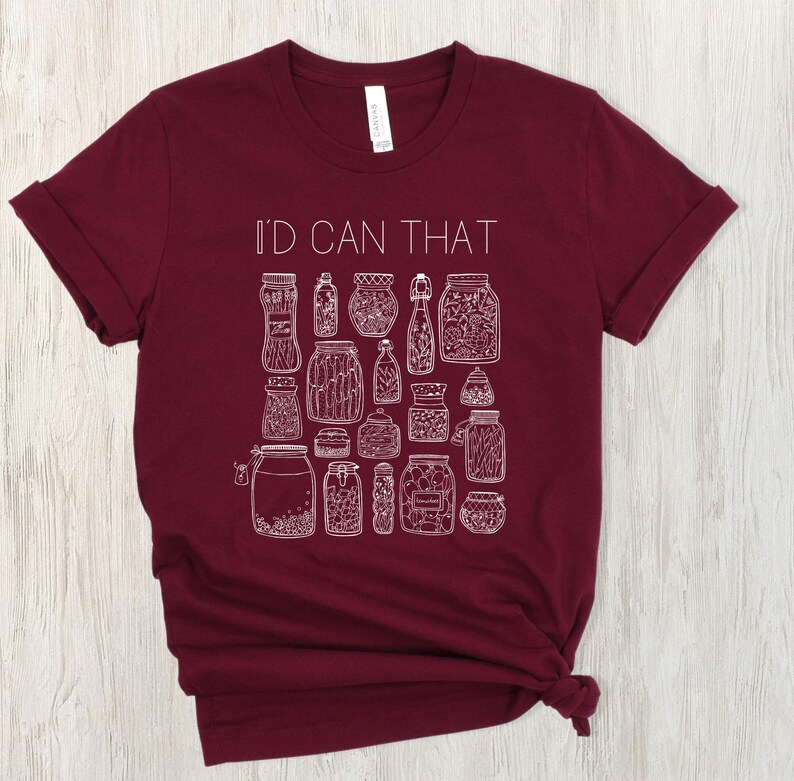 May include: A maroon t-shirt with the text "I'd Can That" in white lettering. The shirt features a design of various jars with different contents, all in white.