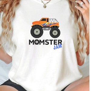 May include: White t-shirt with a graphic of an orange monster truck with blue and yellow accents. The text "MOMSTER JAM" is printed below the truck.