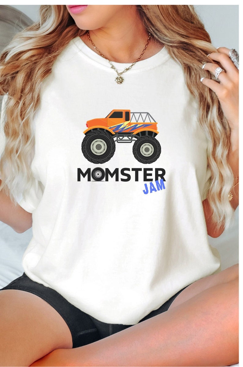 May include: White t-shirt with a graphic of an orange monster truck with blue and yellow accents. The text "MOMSTER JAM" is printed below the truck.