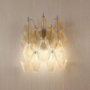 May include: A modern wall sconce with multiple geometric glass shades in a warm amber color. The sconce is made of metal and has a polished chrome finish.