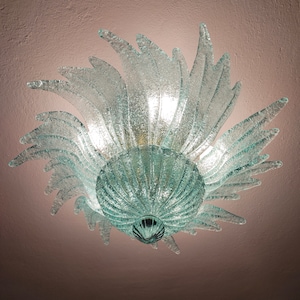 Puede incluir: Una lámpara de techo de vidrio esmerilado con un diseño de estrella. La lámpara tiene una cúpula central y múltiples puntos de vidrio esmerilado que irradian hacia afuera.