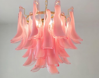 Può includere: Un lampadario di vetro rosa con una struttura in metallo dorato. Il lampadario ha molti petali di vetro disposti a cascata.