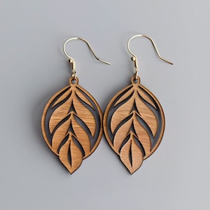 May include: A pair of wooden earrings with a leaf design. The earrings are brown with black accents and have gold hooks.