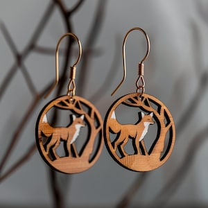 Könnte beinhalten: Ein Paar Holzohrringe mit einem Fuchs-Silhouetten-Design. Die Ohrringe sind braun mit einem weißen Umriss und hängen an goldenen Haken.