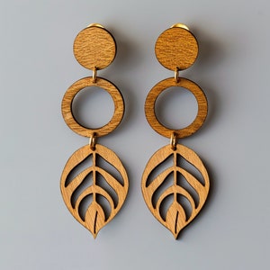 May include: A pair of wooden earrings with a leaf design. The earrings are made of natural wood and have a gold-tone finish. Each earring features a circle and a leaf shape.