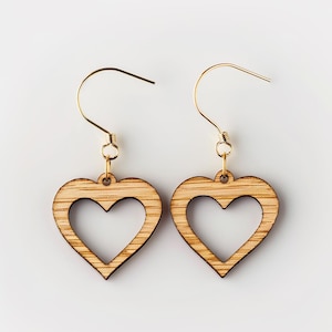 Könnte beinhalten: Ein Paar Ohrringe aus Holz in Herzform mit einem ausgeschnittenen Herzdesign. Die Ohrringe sind aus hellbraunem Holz gefertigt und haben goldfarbene Haken.