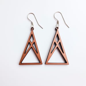 May include: A pair of copper-colored wooden earrings shaped like triangles with geometric cutouts. The earrings have silver hooks.