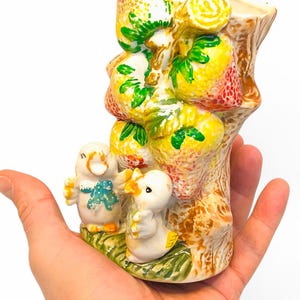 May include: Ceramic vase shaped like a tree trunk with yellow and red strawberries and green leaves. Two white ceramic ducks are at the base of the tree.