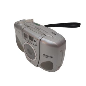 May include: Silver Kodak Advantix C750 camera with a black wrist strap. The camera has a lens, flash, and various buttons. The text "Advantix C750" is printed on the front of the camera.