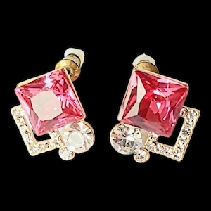 Op de afbeelding: Een paar gouden oorbellen met roze en heldere kristallen accenten. De oorbellen hebben een vierkant roze kristal omgeven door een kleiner vierkant frame van heldere kristallen.