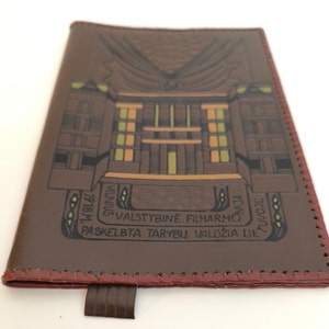 May include: A brown leather notebook cover with a detailed embossed image of a building. The text "VALSTYBINĖ FILHARMONIJA" is embossed on the cover.