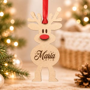 May include: A light brown wooden reindeer ornament featuring a bright red nose, dark brown eyes, and the name Maria engraved in cursive script on its belly. The ornament is suspended by a thin red ribbon attached to the top of its antlers.