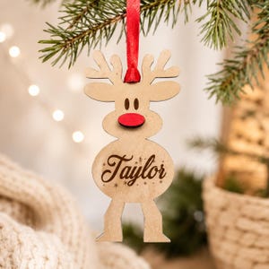 May include: A light brown wooden reindeer ornament featuring a bright red nose and the name Taylor engraved in a cursive script on its belly. The ornament is suspended by a red satin ribbon and includes small engraved snowflake details.