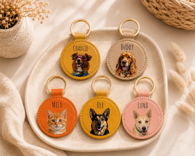 May include: A collection of personalized pet keychains. Each keychain features a circular leather design with a gold-colored ring. The keychains display portraits of dogs and a cat, with names like "Charlie," "Buddy," "Milo," "Rex," and "Luna."