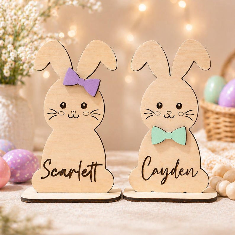 Op de afbeelding: Twee houten paashaasdecoraties. E&eacute;n konijn heeft een paarse strik en de naam "Scarlett" erop geschreven. Het andere konijn heeft een groene strik en de naam "Cayden" erop geschreven. De konijnen staan op een houten voet.