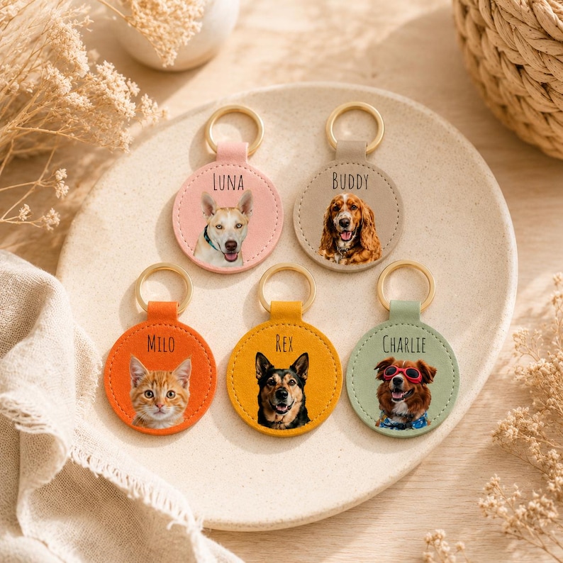 May include: A collection of personalized pet keychains. Each keychain features a circular design with a pet's portrait and name. The keychains are in various colors, including pink, tan, orange, yellow, and green, with gold-colored key rings.
