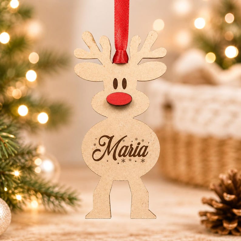May include: A light brown wooden reindeer ornament featuring a bright red nose, dark brown eyes, and the name Maria engraved in cursive script on its belly. The ornament is suspended by a thin red ribbon attached to the top of its antlers.