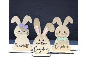 Op de afbeelding: Drie houten konijnenfiguren met beschilderde details. De konijnen staan op sokkels met de namen "Scarlett", "Cayden" en "Cayden" erop.