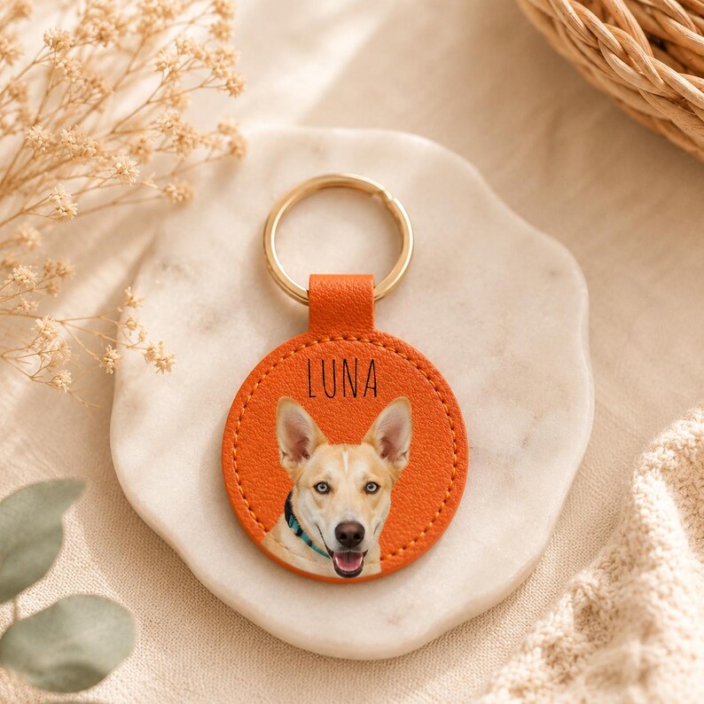 May include: Orange leather keychain with a gold ring. The keychain features a photo of a dog with the name "LUNA" printed in black. The dog has tan fur, a black nose, and blue collar.