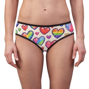 Puede incluir: Ropa interior con base de color crema y un patrón repetitivo de corazones dibujados a mano en varios colores, incluyendo rojo, azul y rayas de arcoíris. La prenda tiene una cintura elástica negra y un borde festoneado negro en las piernas.