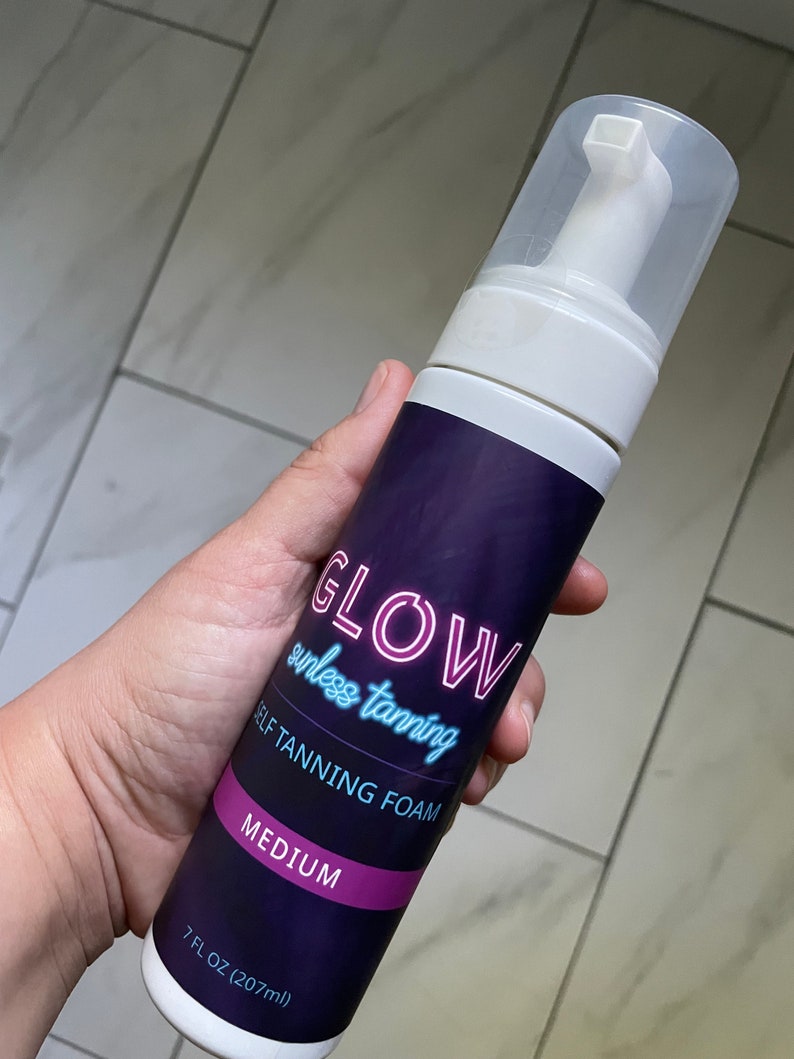 May include: A white bottle of self-tanning foam with a purple label that says "GLOW sunless tanning SELF TANNING FOAM MEDIUM 7 FL OZ (207 ml)".