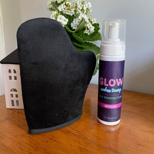 May include: A black self-tanning mitt and a bottle of self-tanning foam labeled "GLOW sunless tanning SELF TANNING FOAM MEDIUM 7 FL OZ (207 ml)"