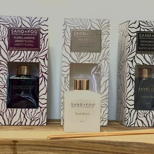 May include: A white ceramic mug with a black handle and the text "But First, Coffee" in a black, handwritten-style font. The mug is on a white surface.