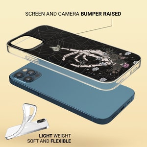 May include: A clear phone case with a black and white design of a skeleton hand reaching out from a spider web. The case has a raised bumper around the camera lens and screen.