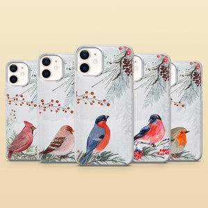 May include: Four phone cases with wintery designs featuring birds and berries. The cases are clear and show the phone's design through the back. The birds are a cardinal, a blue jay, a robin, and a goldfinch.