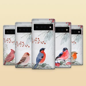 May include: A collection of five phone cases featuring watercolor illustrations of various birds. Each case showcases a different bird species perched on a branch with red berries and a snowy background. The cases have a white base.