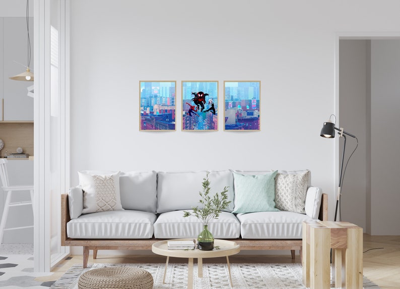 May include: Three framed prints of a comic book style illustration of Spider-Man characters swinging through a city skyline. The prints are hung on a white wall above a light-colored couch in a living room.