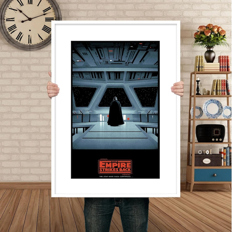 May include: A framed poster of the Star Wars movie "The Empire Strikes Back". The poster features a dark silhouette of Darth Vader standing in the bridge of the Death Star. The text "Episode V: The Empire Strikes Back" is printed in red on a black background.