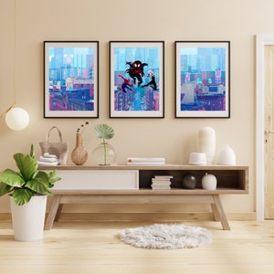 May include: Three framed prints of a comic book style illustration of Spider-Man characters in a city setting. The prints are hanging on a light beige wall above a wooden shelf with a white top.