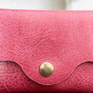May include: A pink leather wallet with a gold button closure and the number "8592" embossed on the front.