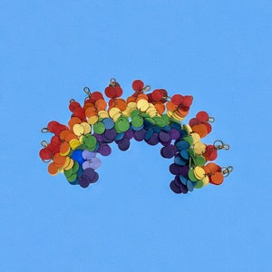 May include: A rainbow-colored garland made of small, round, wooden discs. The garland is arranged in a semi-circle shape, with the colors of the rainbow arranged in order from red to violet.